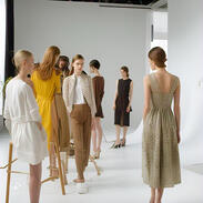 Models getting their hair fixed and trying outfits in an open, bright studio, hinting at spontaneity and craftsmanship.